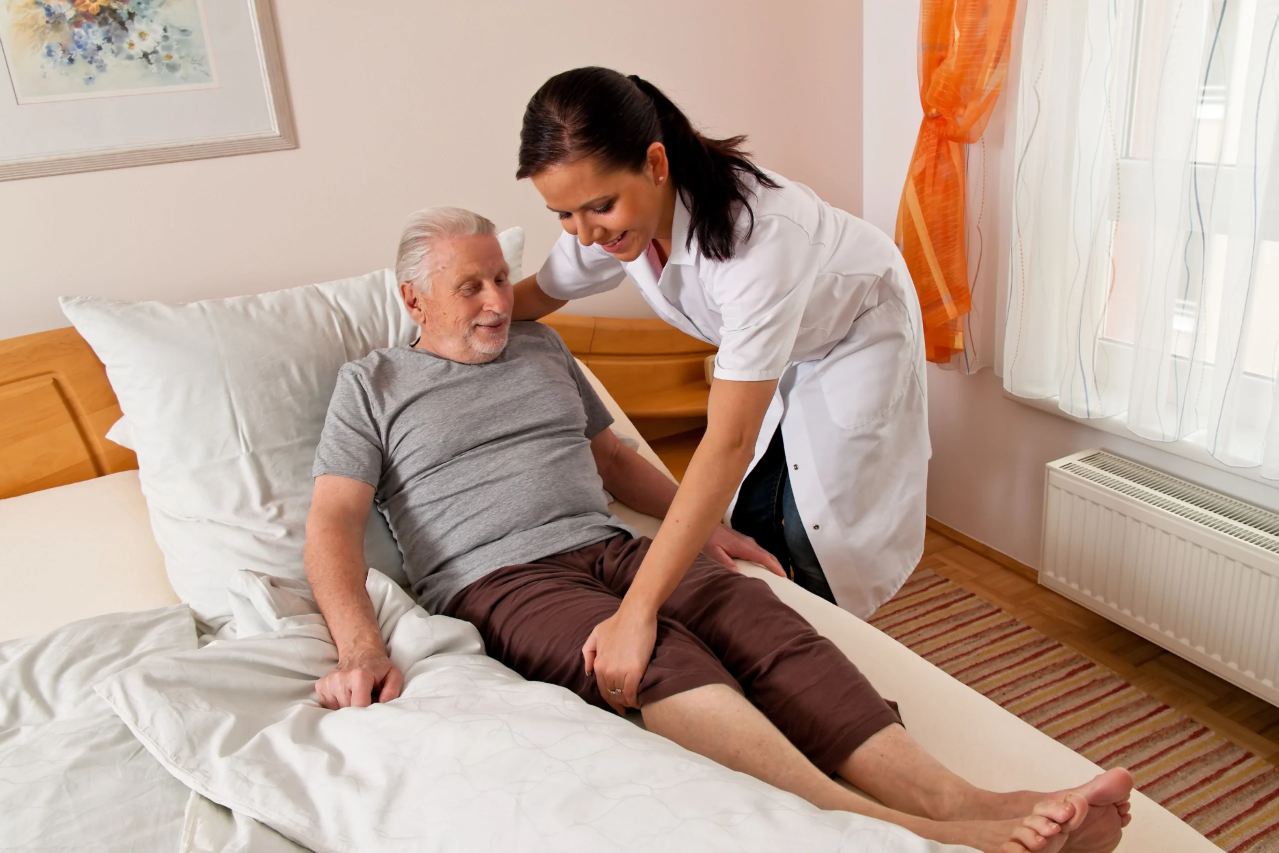 Senior man being helped out of bed by a caregiver.