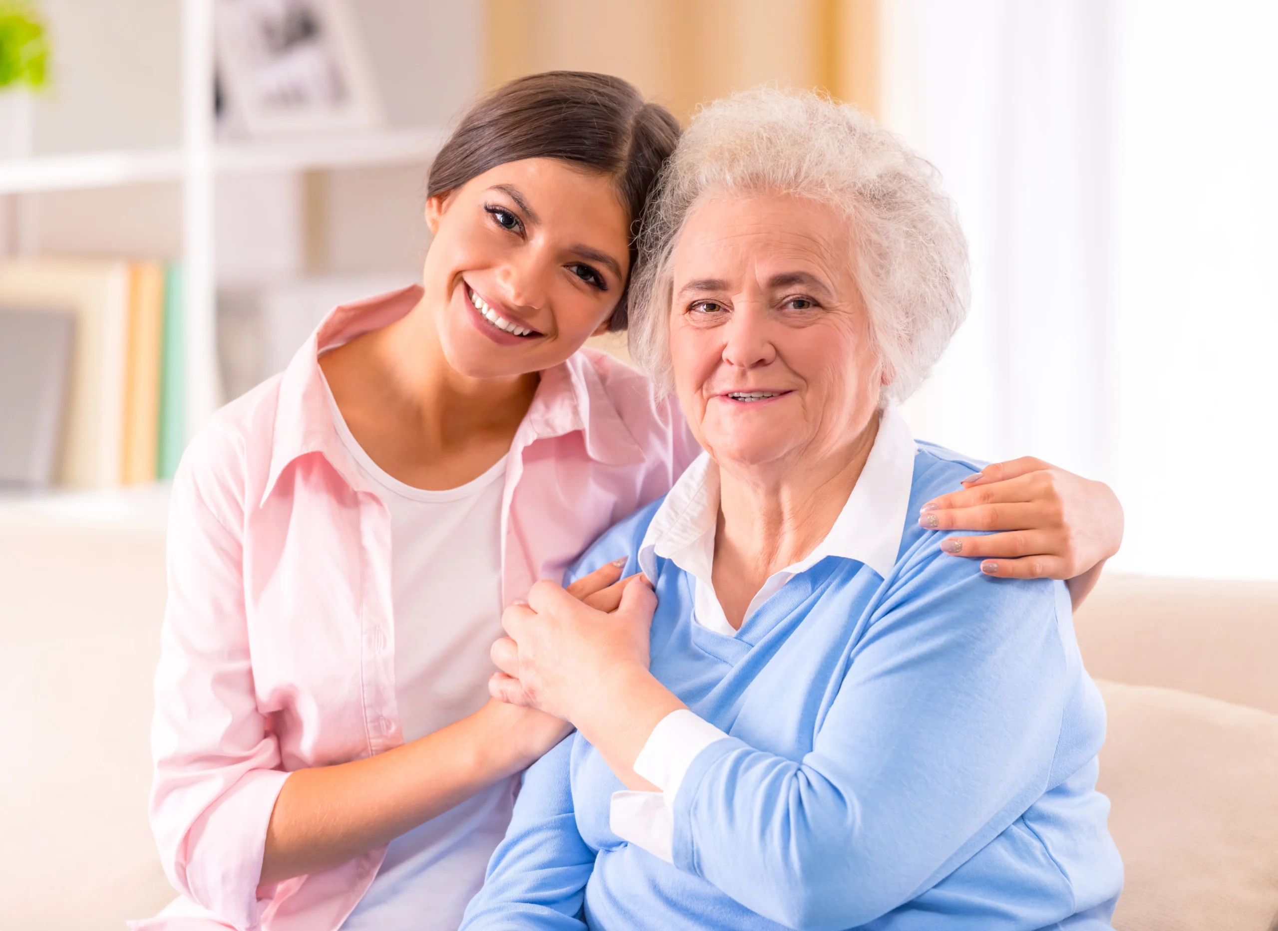 Younger woman embracing senior woman as both are seated together.