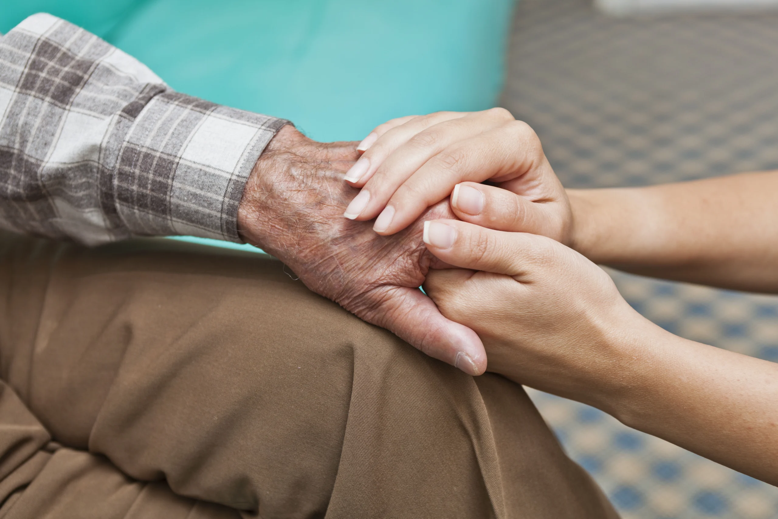 Closeup of senior man's hand being held by a younger person.